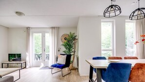 Ett modernt vardagsrum med en matplats, en tv, en växt och stora fönster.
