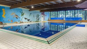 En inomhuspool med en väggmålning som föreställer marint liv, en fri utsikt över utomhusmiljön genom stora fönster och en blå, vadderad bänk längs poolkanten.