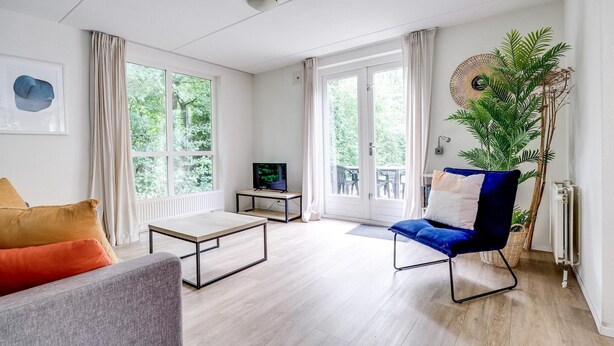 Ett modernt vardagsrum med en soffa, en blå fåtölj, ett soffbord och en tv som står på ett tv-bord.