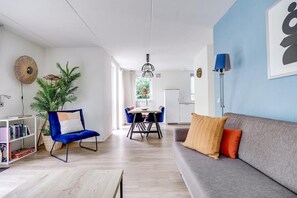 Ein modernes Wohnzimmer mit einer Couch, einem blauen Sessel, einem Esstisch und einem Bücherregal.