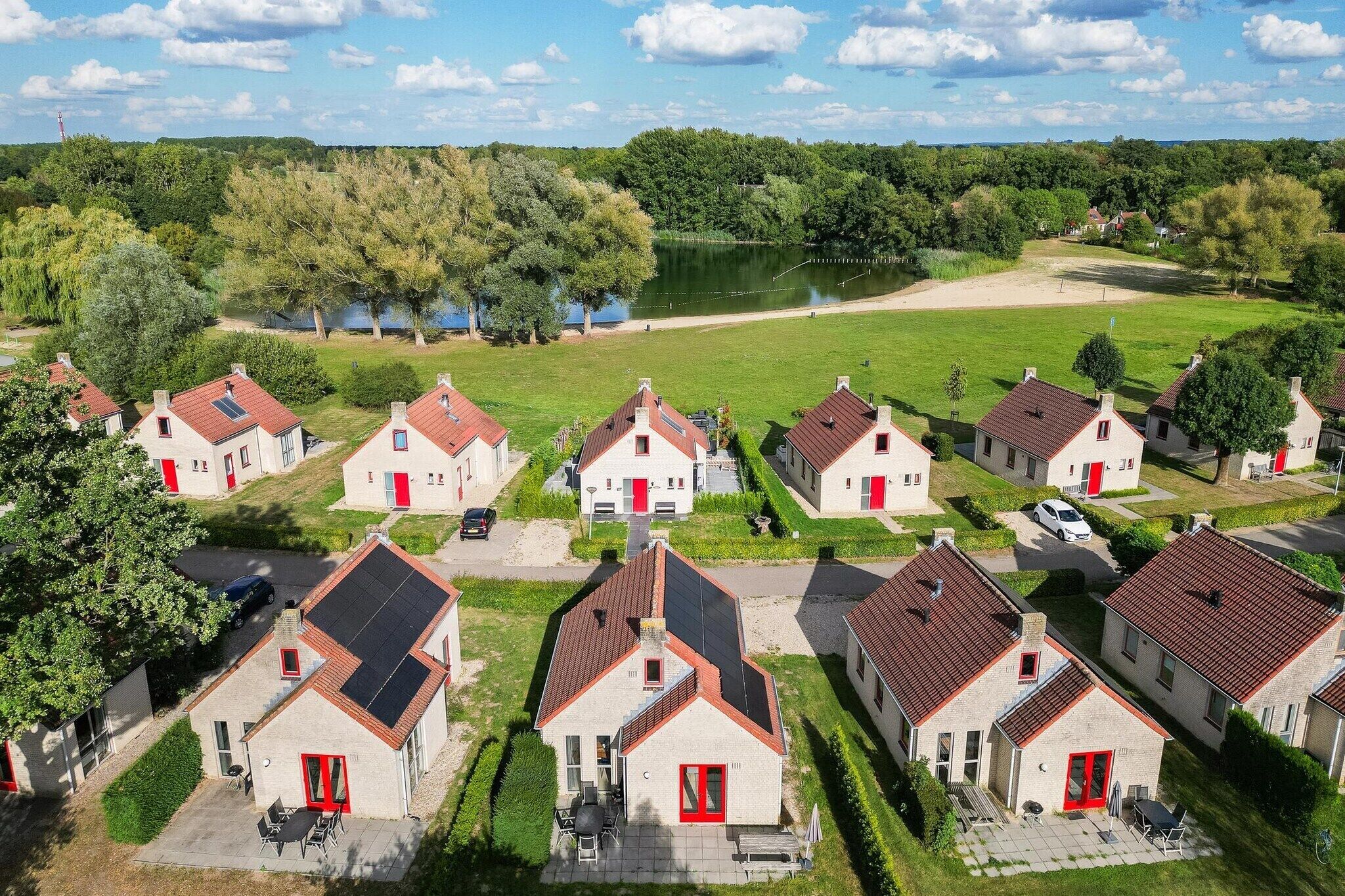 Zona residencial con casas que tienen puertas rojas y paneles solares, rodeada de vegetación y un lago.