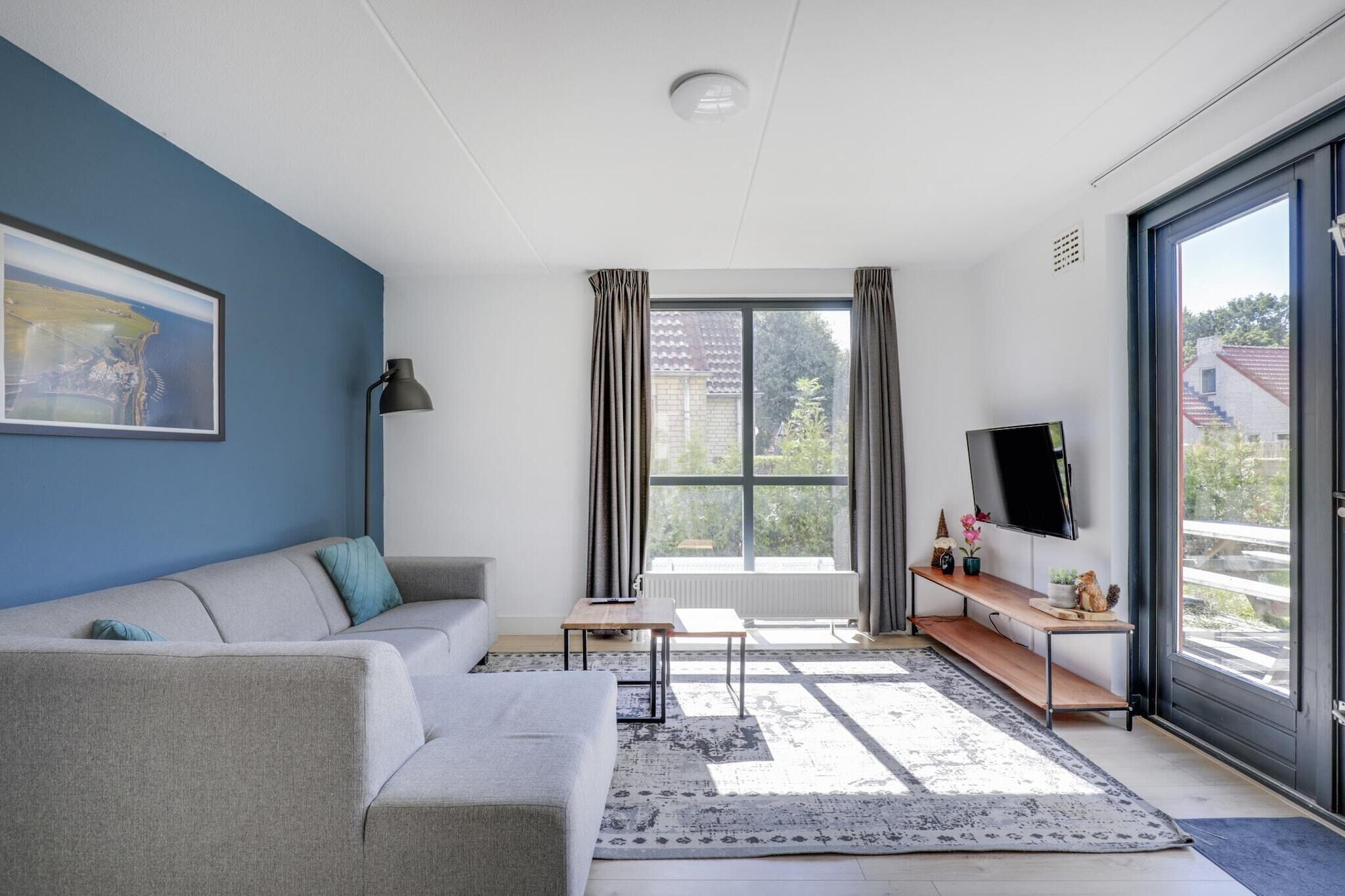 A modern living room with a sofa, a coffee table, a TV, and a large window with curtains.