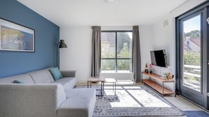 Un salon moderne avec un canapé, une table basse, un téléviseur et une grande fenêtre avec des rideaux.