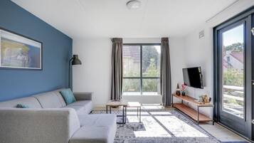 A modern living room with a sofa, a coffee table, a TV, and a large window with curtains.