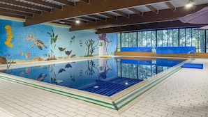 Une piscine intérieure ornée d’une fresque représentant la vie aquatique, dotée d’un plongeoir et offrant une vue sur les arbres à travers de grandes fenêtres.