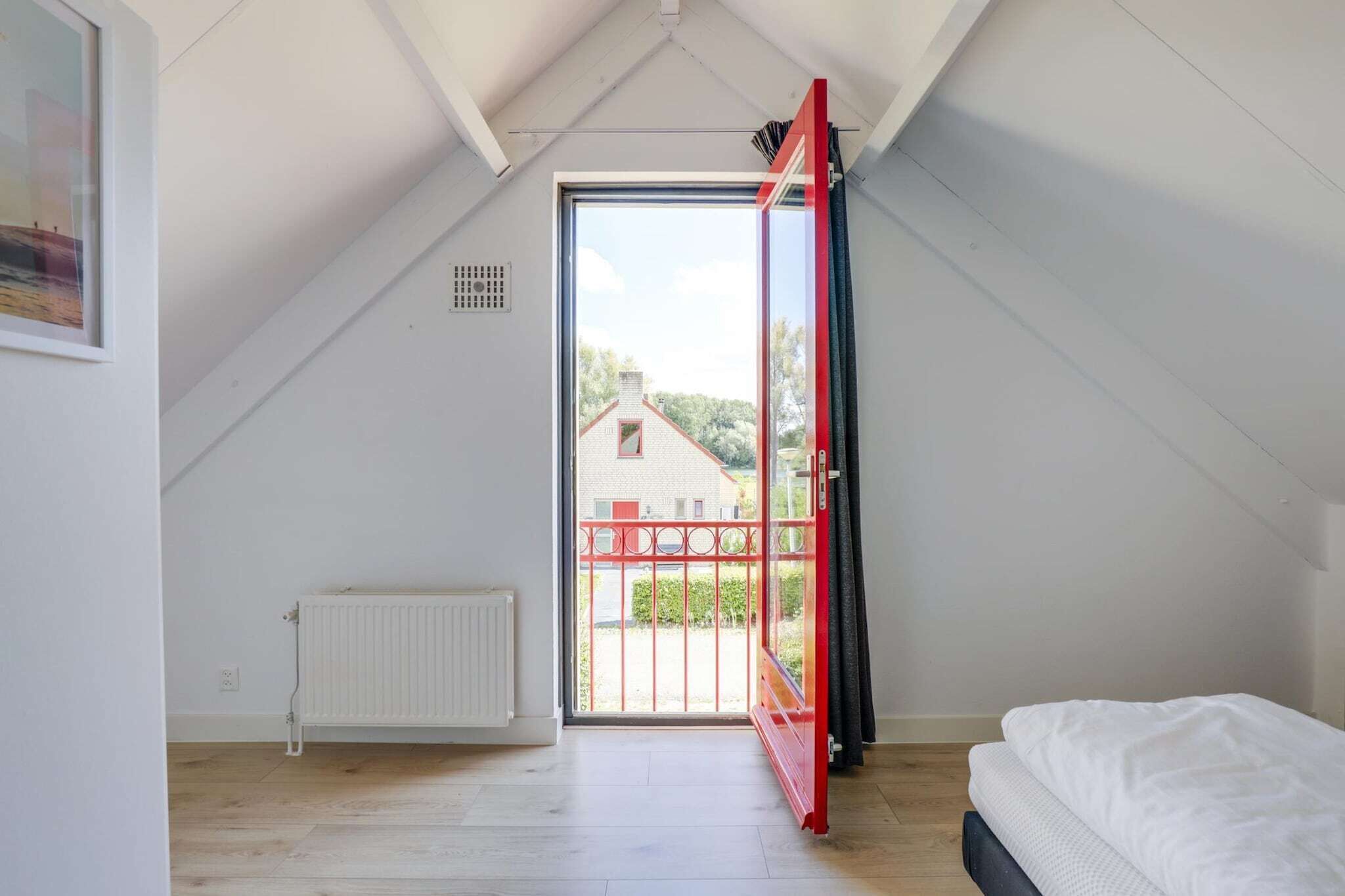 A room with a sloped ceiling, a bed, a radiator, and a door leading to an outdoor area.
