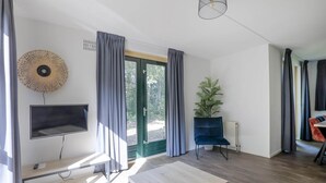 Una sala de estar moderna con televisor de pantalla plana, una mesa de centro de madera, una silla azul, una planta en maceta y un ventanal con cortinas.