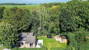 Ein Haus, umgeben von dichtem Baumbestand, mit erkennbarem Dach und einem kleinen, eingezäunten Bereich.
