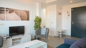 Un salon moderne avec un téléviseur à écran plat, un fauteuil gris, un canapé bleu et une petite table blanche.