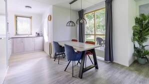Une cuisine moderne avec des meubles blancs, une table à manger entourée de chaises bleues et une grande fenêtre agrémentée de rideaux.