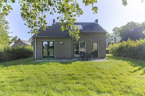 A small brick house with a tiled roof, a front door, and a patio with chairs. - 4-Person Forest Bungalow in Ewijk (Ewijk)