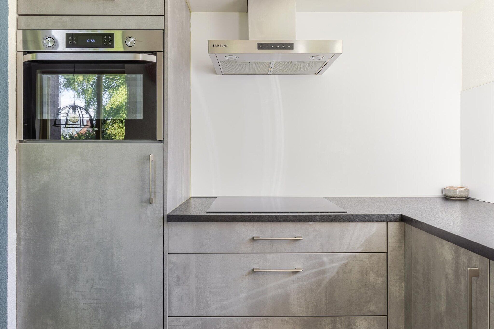 A kitchen with a built-in oven, stainless steel range hood, and grey cabinetry.