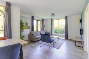 A modern living room with a sofa, a dining table, a chair, and a TV. - 4-Person Forest Bungalow in Ewijk (Ewijk)