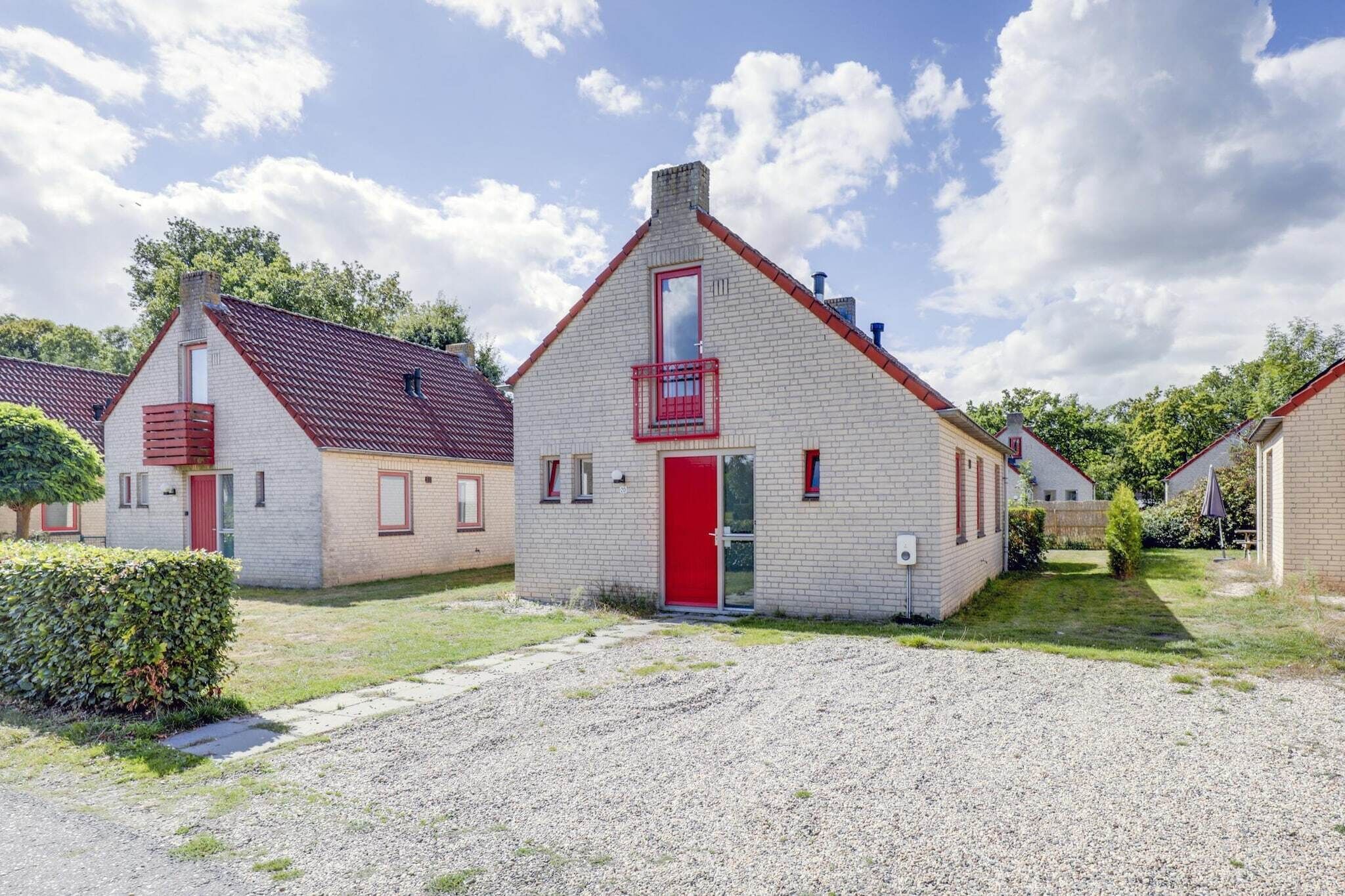 Une rangée de petits bâtiments à un seul étage, avec des portes et des fenêtres rouges, une allée gravillonnée et un ciel dégagé.