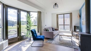 Een moderne woonkamer met grote ramen, een bank, een fauteuil, een tafel en een open haard.