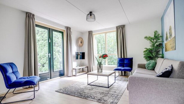 Un salon moderne avec un canapé, un fauteuil bleu, une table basse et un téléviseur.