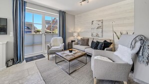 Un salon moderne avec un canapé, un fauteuil, une table basse et une vue à travers une porte-fenêtre coulissante.
