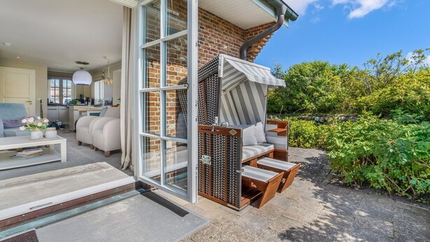 Een modern huis met een glazen deur die leidt naar een woonruimte, een terras met tuinmeubilair en een gevel van baksteen.