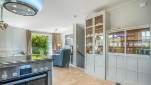 Een moderne keuken met een inbouwoven, een eethoek met uitzicht op groen, en een glazen kast met servies.