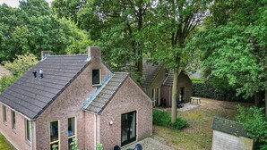 Une maison en briques avec un toit en pente, un petit patio avec une table et des chaises, et un abri de jardin dans la cour.