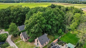 Une vue aérienne d’un quartier résidentiel, avec des maisons entourées d’arbres denses, une route bien visible et des champs ouverts en arrière-plan.