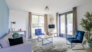 Un salon moderne comprenant un canapé, deux fauteuils, une table basse, un téléviseur et une grande fenêtre avec des rideaux.
