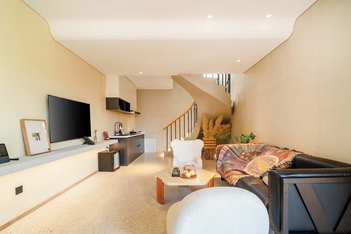 A modern living room with a sofa, a coffee table, a TV, and a staircase leading to an upper level.