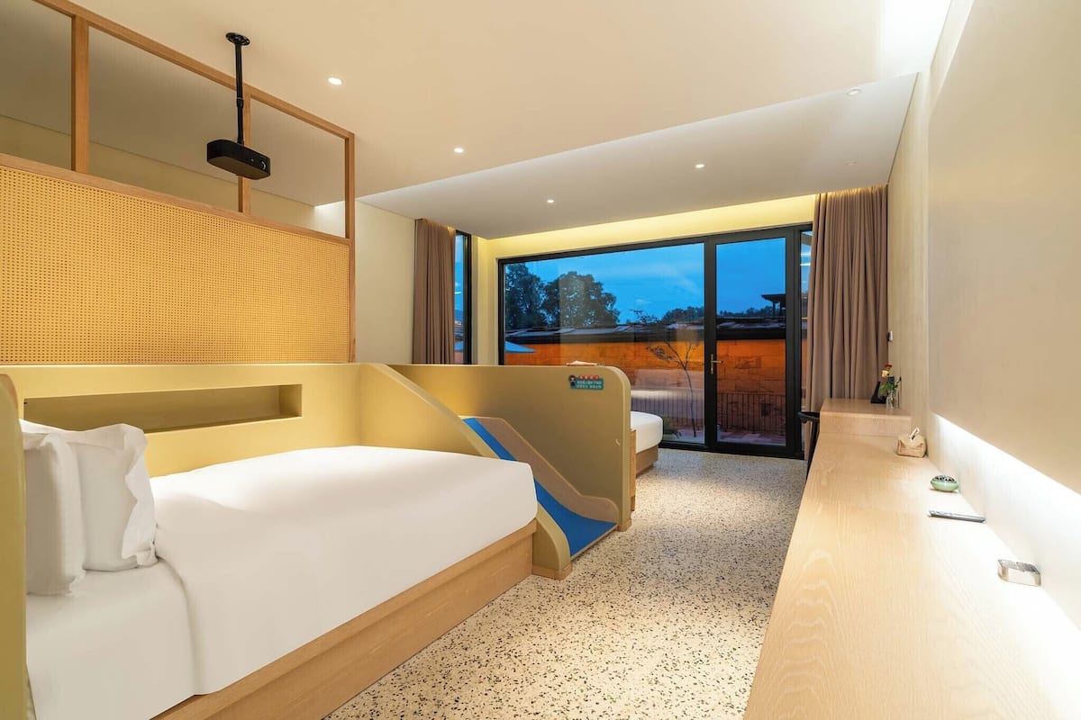 A hotel room with a bed, a desk, a chair, a large window with a view, and a ceiling light.