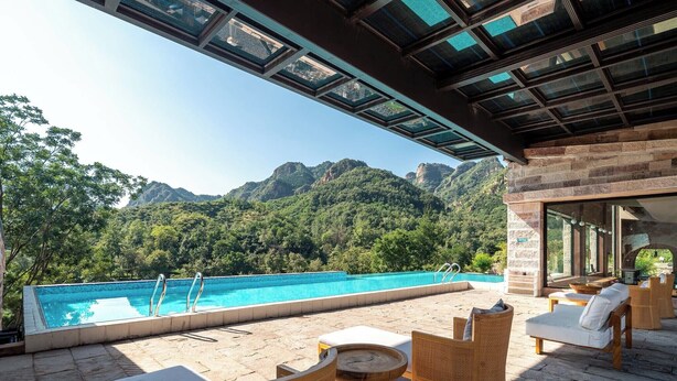 A rooftop pool with a view of mountains, wicker furniture, and a glass-enclosed area. - Manning Retreat (Handan)