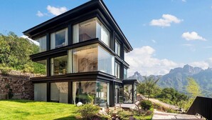 A modern two-story house with large glass windows, a stone retaining wall, and a view of mountains. - Manning Retreat (Handan)