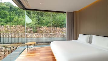 Camera d'albergo moderna con un letto grande, un tavolino e vista su un muro di pietra e vegetazione.