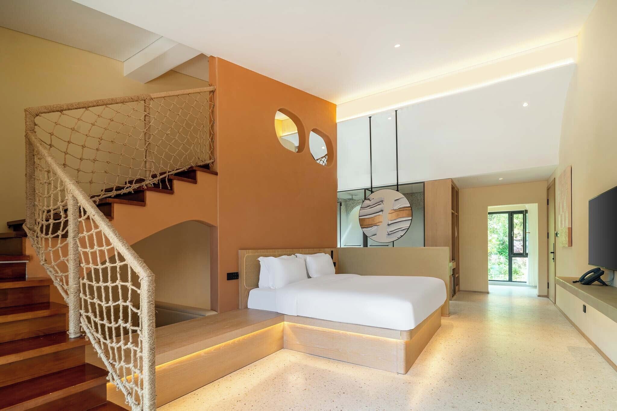 A modern bedroom with a bed, a staircase with a rope net, and a view to the outside.
