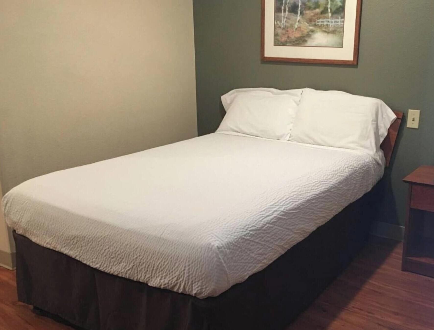 Un letto singolo con copripiumino bianco e gonna a terra scura.