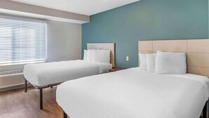 Una habitación de hotel con dos camas, una ventana con persianas, un calentador y una pared de acento color aguamarina.