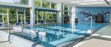 Una piscina interior con paredes de vidrio transparente, paredes de azulejos azules y suelo de baldosas.