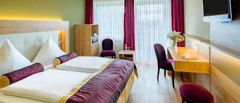 Una habitación de hotel con cama, escritorio, silla, televisor y ventana con cortinas.