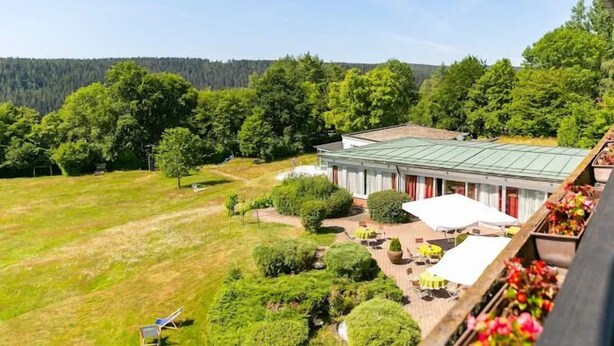 Een hotel met een groen dak, terras buiten en uitzicht op een bebost gebied.