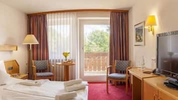 A hotel room with a bed, TV, two chairs, a small table, and a balcony.
