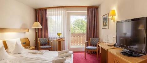 Une chambre d’hôtel avec un lit, une télévision, deux chaises, une petite table et un balcon.