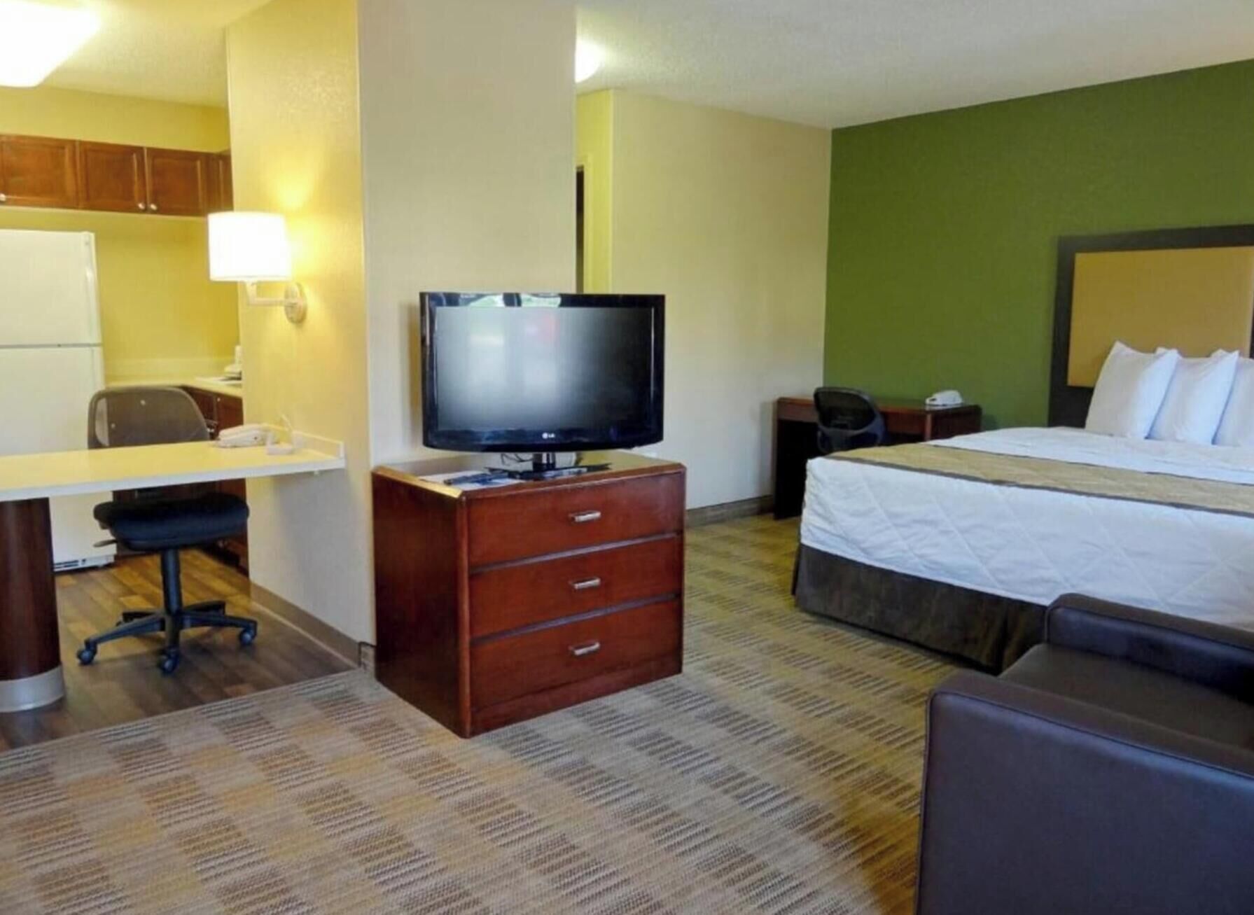 A hotel room with a bed, a desk with a chair, a television, and a small cabinet.