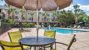 Zona junto a la piscina con mesa y sillas, una piscina y un edificio al fondo.