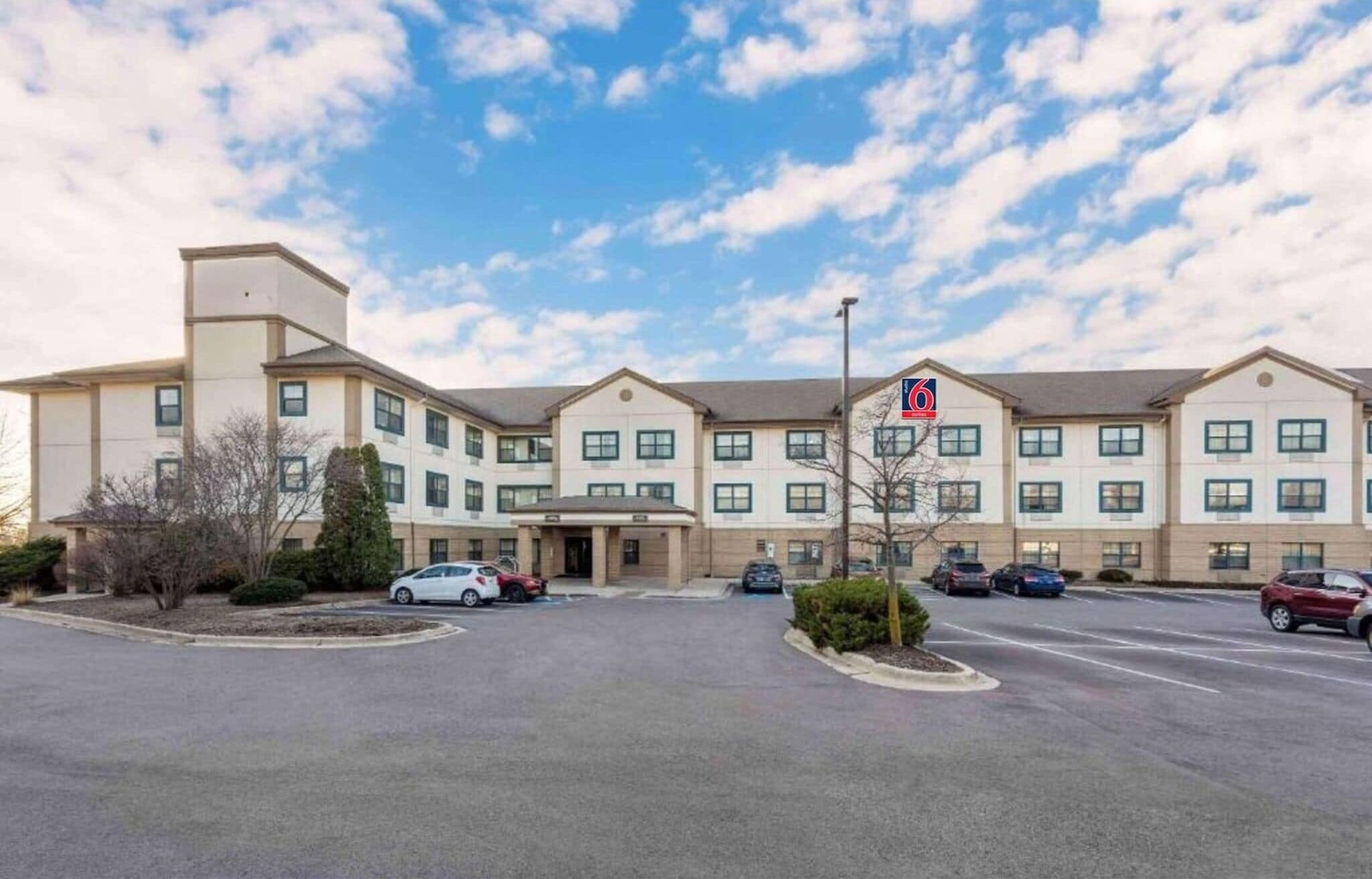 Een meerhoog hotel met een parkeerplaats, een heldere lucht en een bord waarop een 6-sterren beoordeling staat.