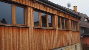 Ein Holzhaus mit mehreren Fenstern, einem Steinfundament und einer Satellitenschüssel.