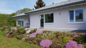 Ein modernes Haus mit Ziegeldach, großen Fenstern und einem Garten mit verschiedenen Blumen.