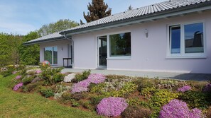 Ein modernes Haus mit Ziegeldach, großen Fenstern und einem Garten mit verschiedenen Blumen.