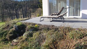 Ein modernes Haus mit Terrasse, zwei Liegestühlen und einem Garten.