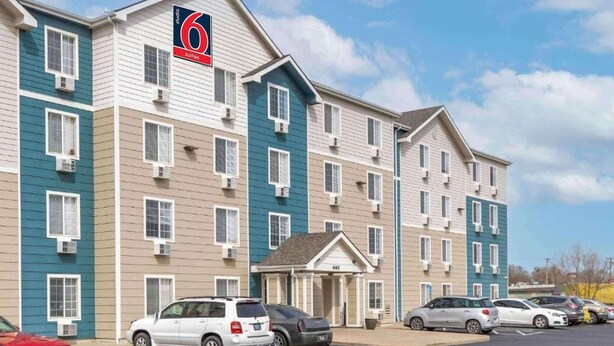 A multi-story hotel with a prominent '6' sign, multiple parking spaces, and a small entrance building. - 1 Full Bed | Mobil Acc RI Shwr Nsmk Kitchen (Wichita KS)