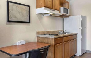 A compact kitchen with wooden cabinets, a white refrigerator, a microwave, and a small dining table with a chair.