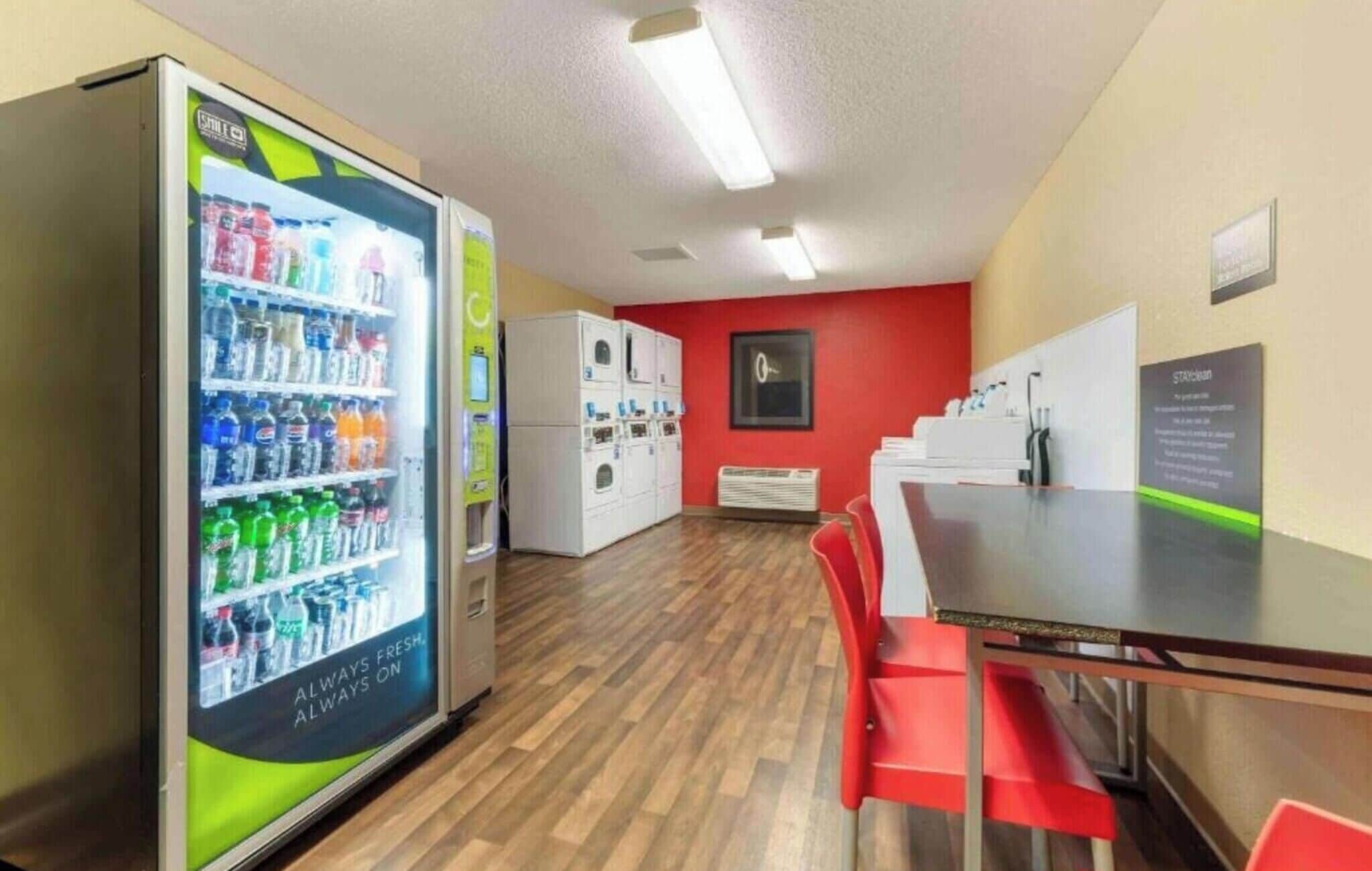 Ein Zimmer mit einem Automaten, einer roten Wand, einem weißen Heizkörper und einem Tisch mit Stühlen.