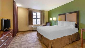 A hotel room with a bed, a television, a desk, and a window with curtains.